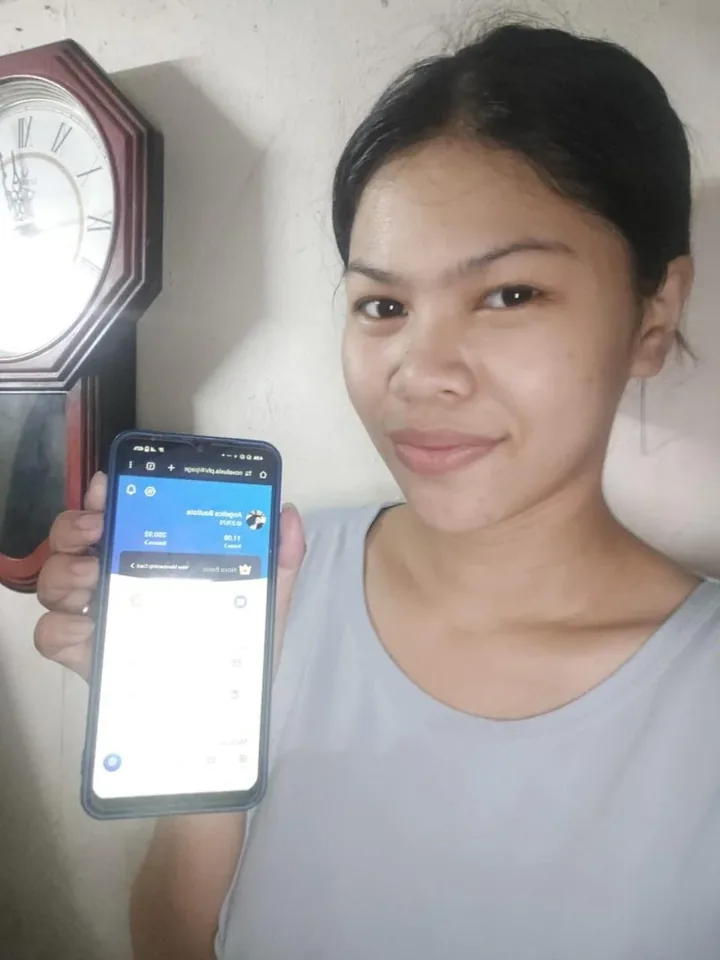 A woman beside a wall clock holding up a phone on the account screen, points and balance in view, the account detail novaluxia reviews should show