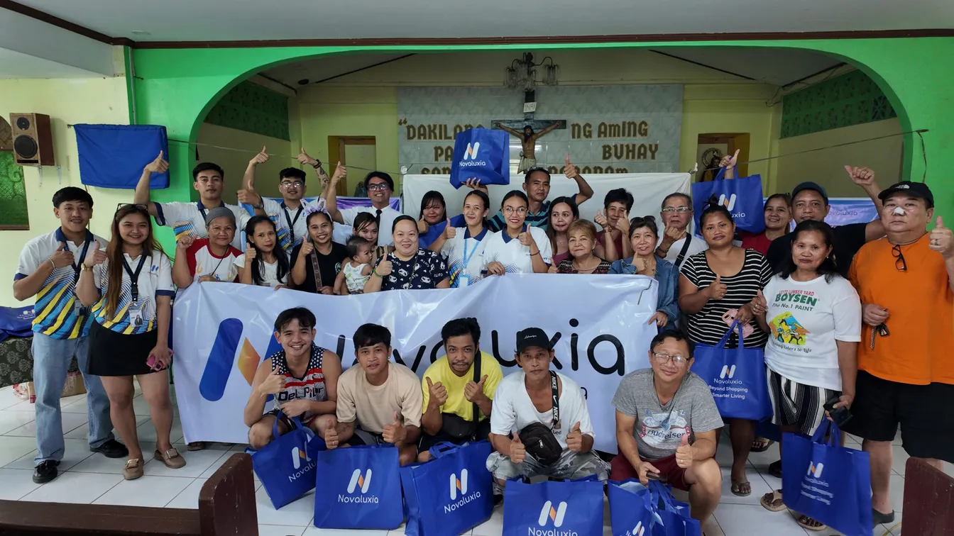 About forty Novaluxia PH community members posing behind a branded banner with blue tote bags
