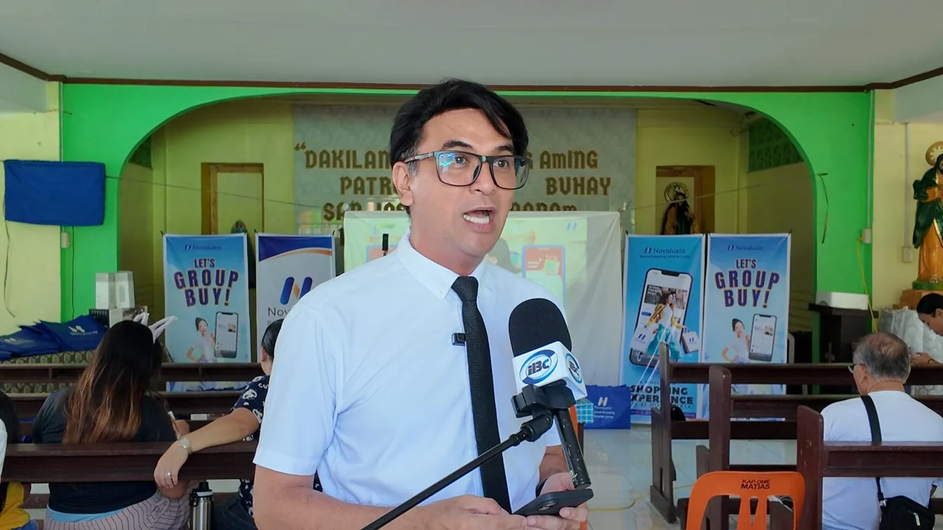 Novaluxia PH group-buy orientation session with a speaker at the microphone and posters behind him